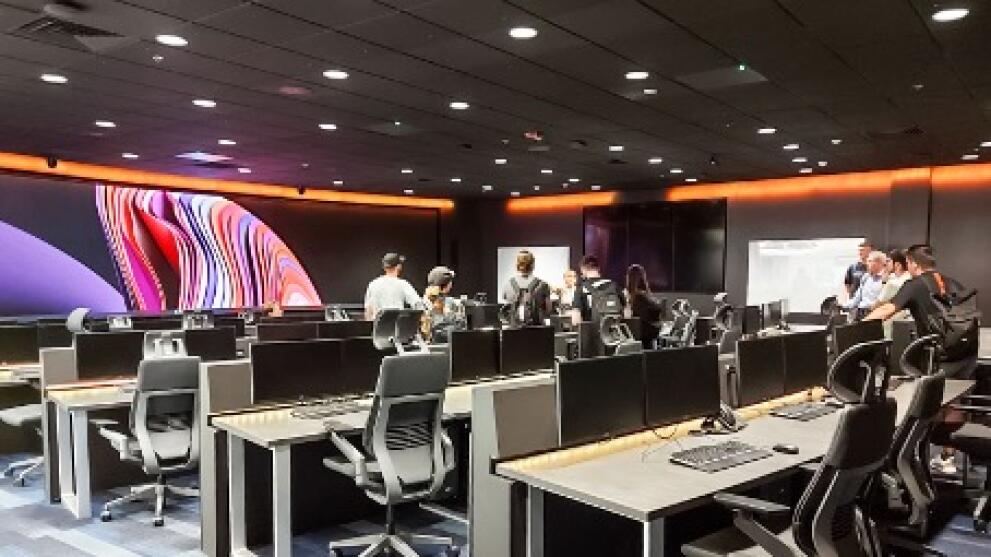 A dimly lit room with lots of computer workstations and large screens.