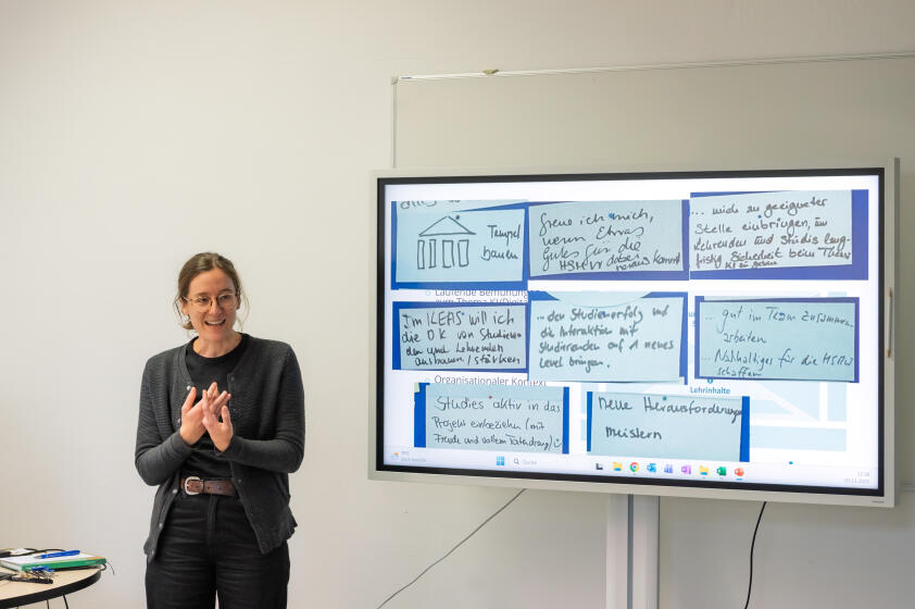 Schwarz gekleidete Frau neben großem Bildschirm mit Powerpoint-Präsentation