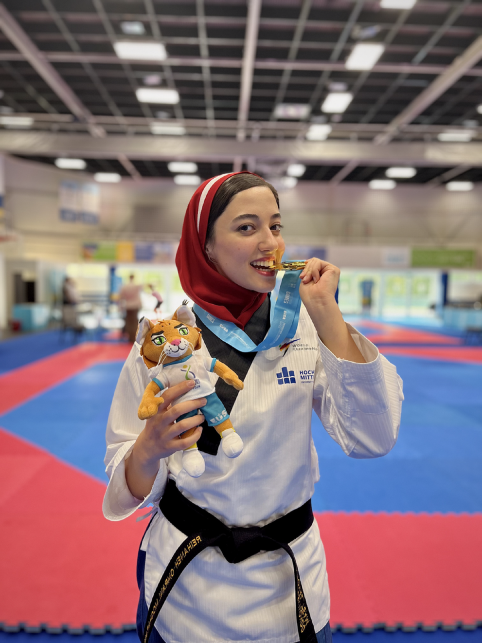 A taekwondo fighter wearing the HSMW logo bites into a medal.