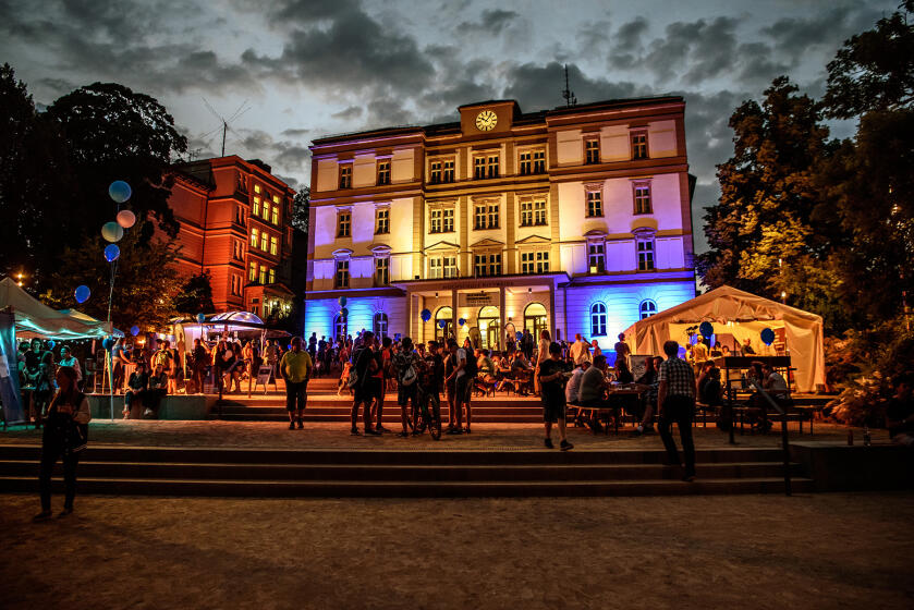 Beleuchtetes historisches Gebäude bei Nacht mit Menschenmenge davor und bunten Lichtern